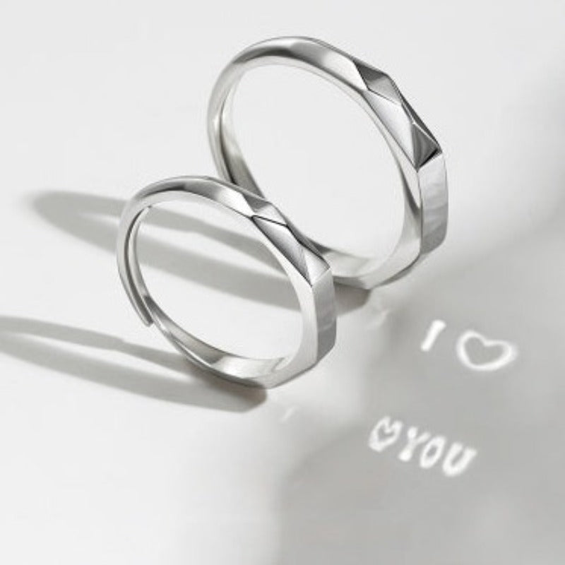 Two S925 Sterling Silver Light Reflection Rings by Jingqian with a faceted design are placed on a white surface. Light reflecting off the rings casts a shadow with the words "I â¤ï¸ YOU" below them.